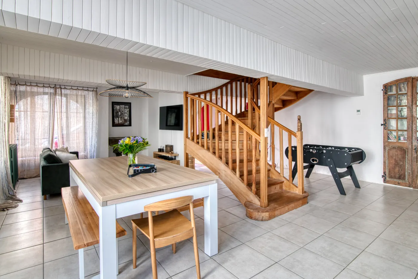Séjour du 23 avec grande table, baby-foot et escalier en bois
